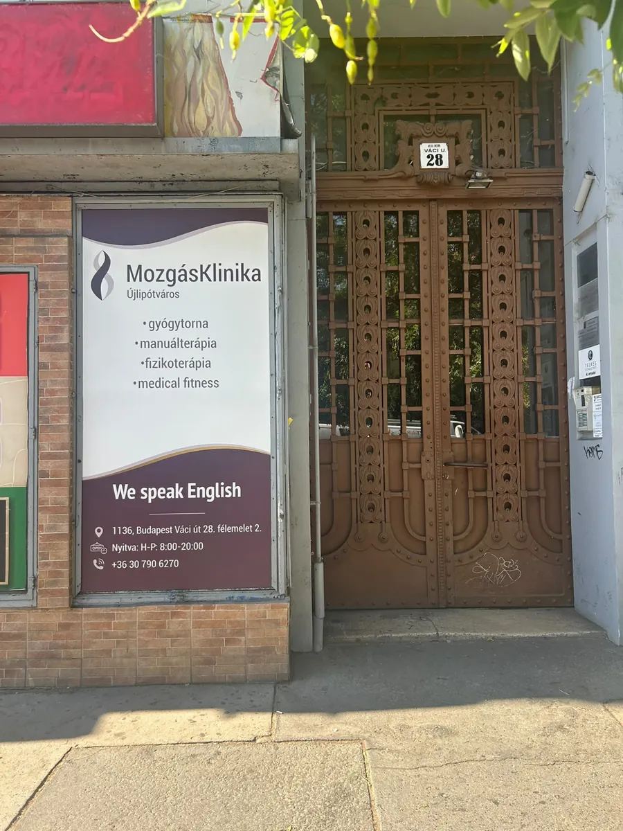 A Váci út 28. utcai bejárata: díszes, barna kovácsoltvas kétszárnyú kapu a házszámtáblával, tőle balra a kirakatban a MozgásKlinika Újlipótváros plakátja